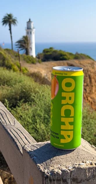 A Mango Green can on a stone wall with a lighthouse and the ocean behind it