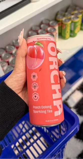 A hand holding a Peach Oolong can in a shop, above a blue shopping basket